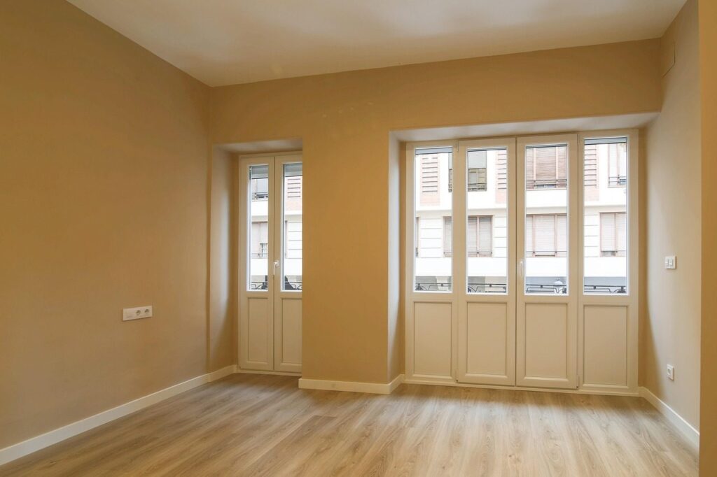 Pièce d'appartement vide avec parquet clair, murs beiges et portes-fenêtres, prête pour un état des lieux
