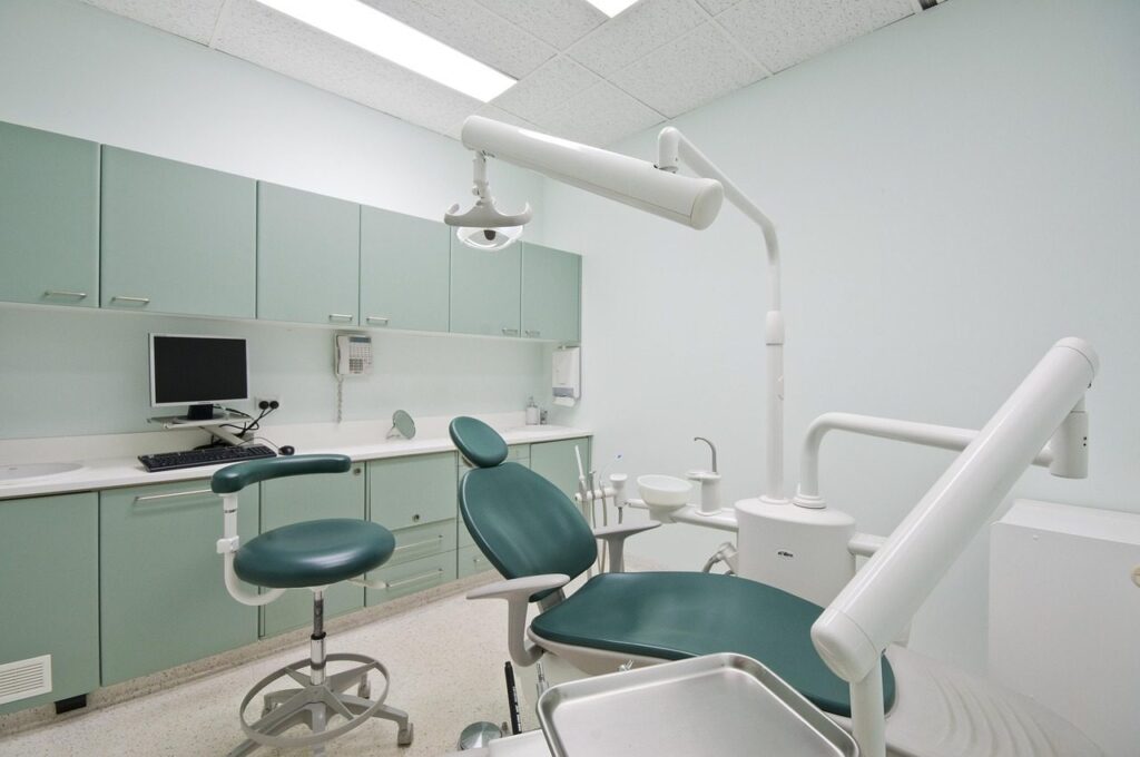 Cabinet dentaire avec fauteuil de soins vert, tabouret du praticien et poste informatique