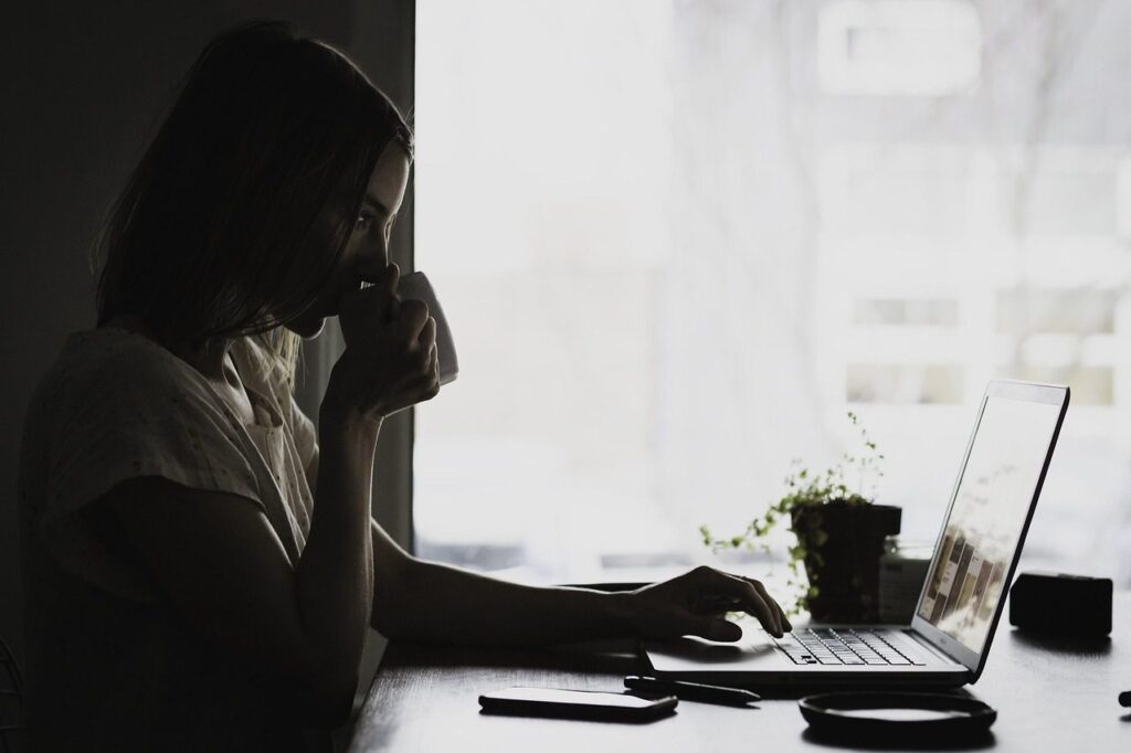 Indépendante buvant un café devant son ordinateur portable, à son bureau près d'une fenêtre