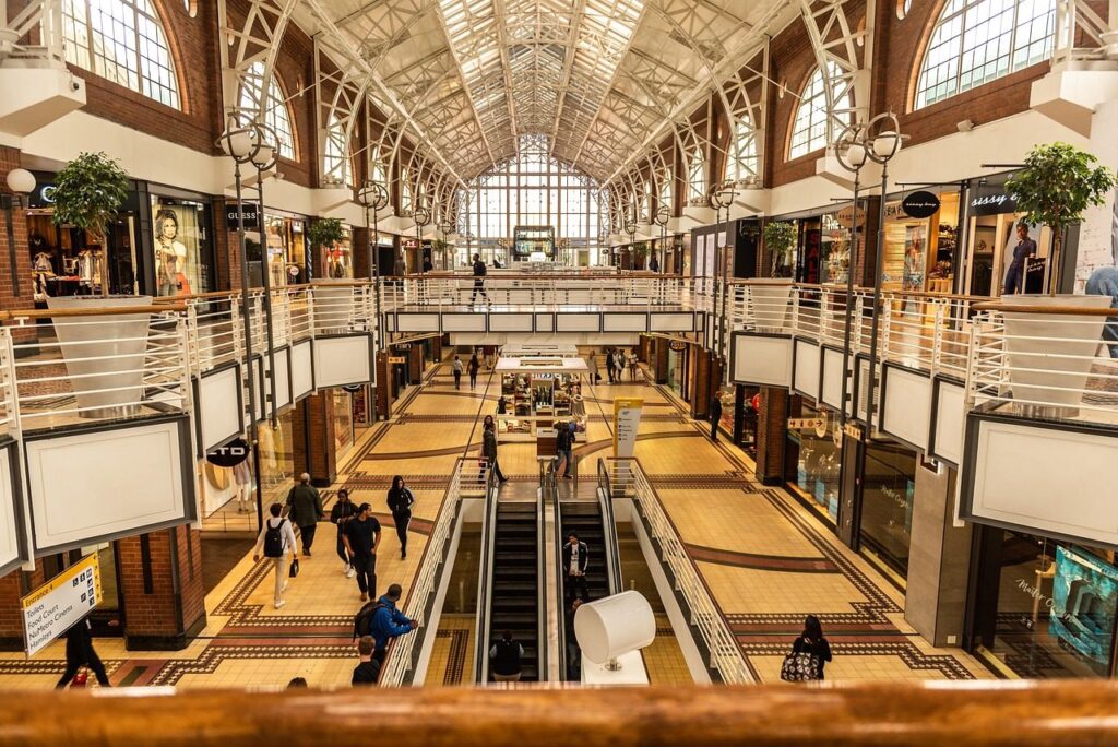 Galerie marchande sous verrière avec boutiques sur deux niveaux et escalators