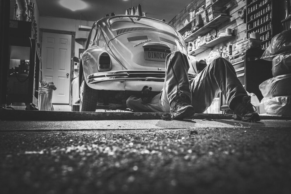 Mécanicien allongé sous une voiture ancienne dans un garage, photo en noir et blanc