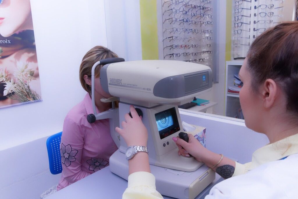 Opticienne mesurant la vue d'une cliente avec un autoréfractomètre, présentoir de lunettes en arrière-plan