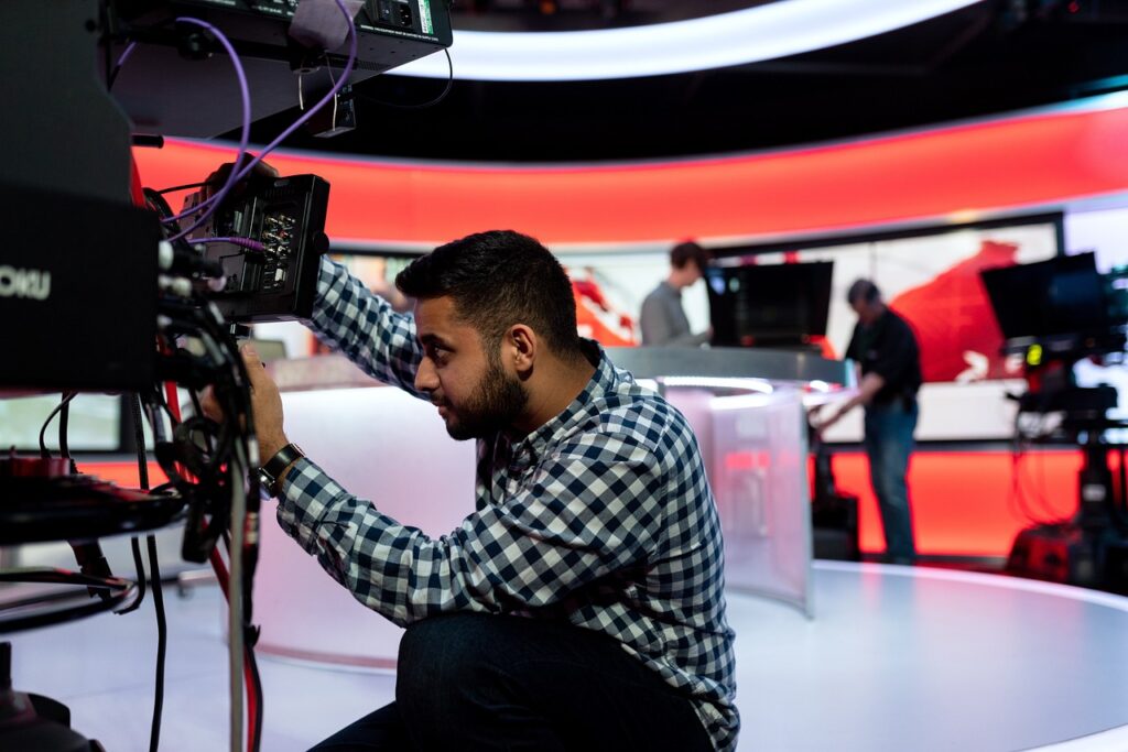Technicien réglant une caméra sur un plateau de télévision au décor rouge et blanc
