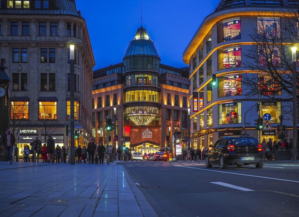 Rue commerçante au crépuscule, bordée d'immeubles aux vitrines éclairées