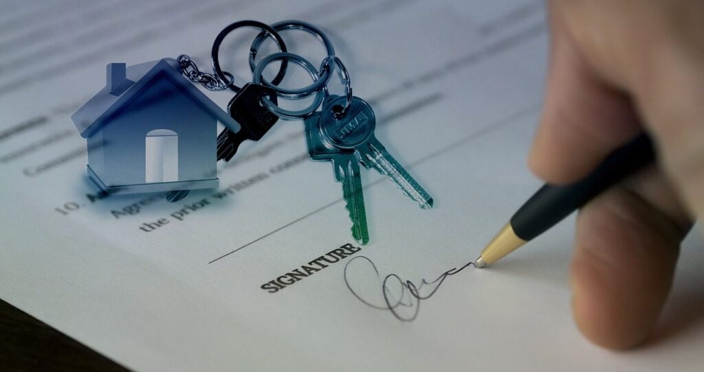 Main signant un contrat de location, clés et porte-clés en forme de maison posés sur le document